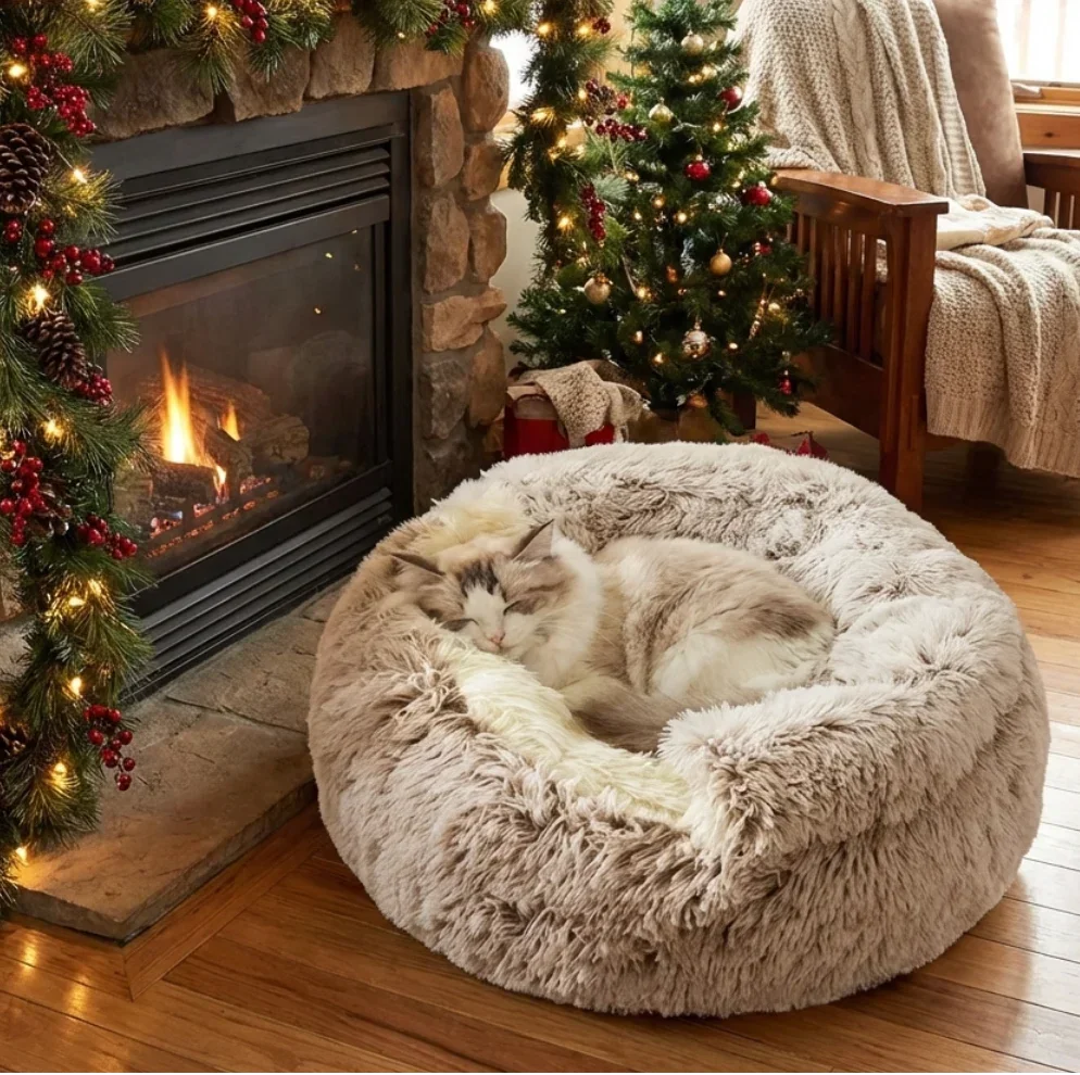 Cat sleeping inside a beige fluffy cozy cocoon bed next to a Christmas fireplace and decorated tree in a warm holiday living room
