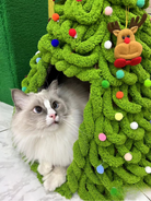 White cat peering out from the Christmas tree-shaped cat bed with a close-up view of festive details.