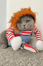 Grumpy-looking cat wearing a Chucky costume with a wig and holding a toy knife.