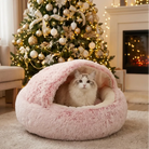 Cat resting inside a pink fluffy cozy cocoon bed in a warm Christmas living room with a decorated tree and fireplace